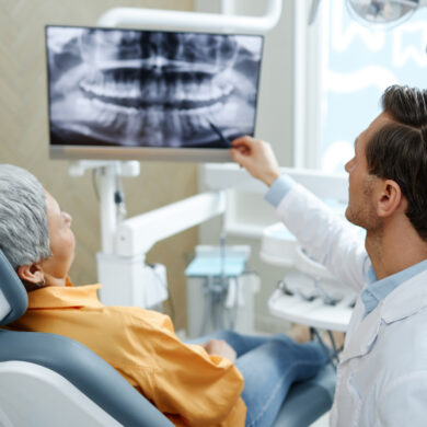 Back view of a dentist pointing at tooth X-ray image on screen during consultation in modern dental clinic